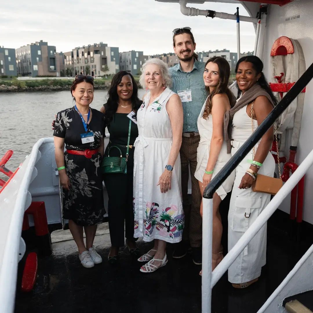 Chris Gittings with six guests on the deck of the Ben Franklin Yacht at sunset, Delaware River behind them