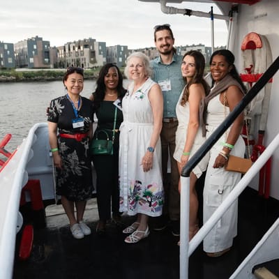 Chris Gittings with six guests on the deck of the Ben Franklin Yacht at sunset, Delaware River behind them