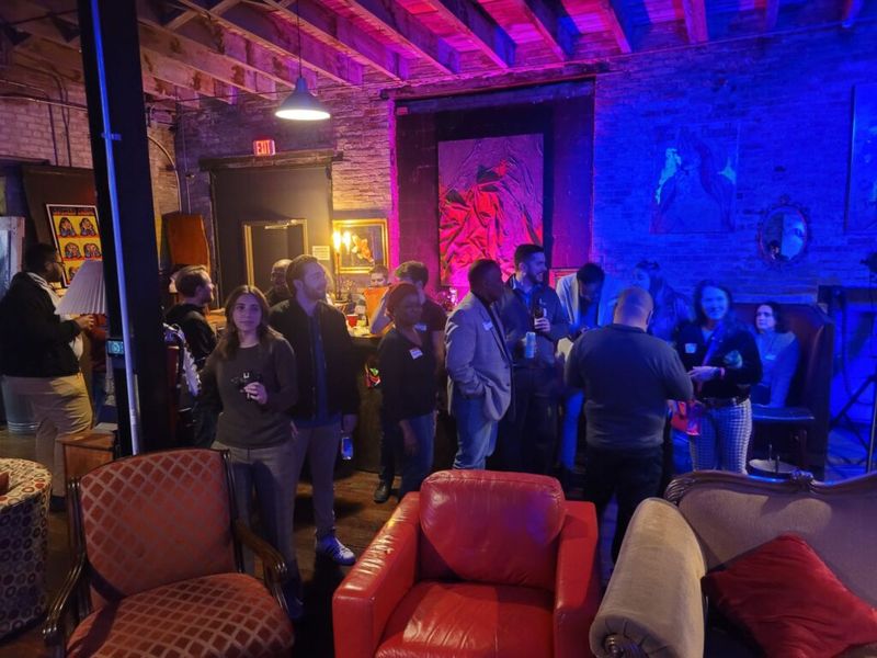 Attendees mingling at a networking event inside a dimly lit brick-walled venue with blue and red ambient lighting