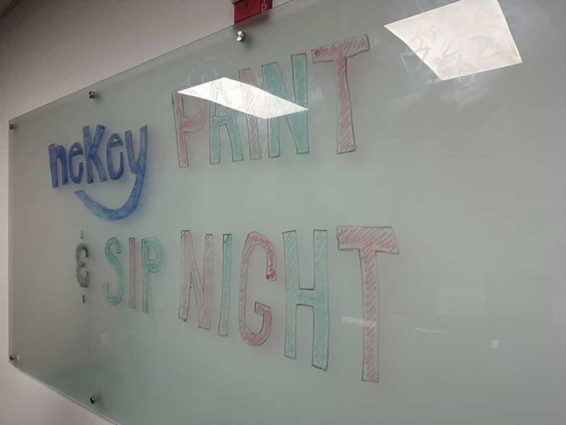 Glass whiteboard with "neKey Paint and Sip Night" written in colorful marker lettering, with the neKey logo in blue on the left