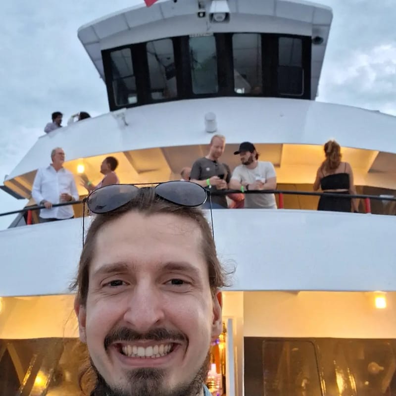 Chris Gittings taking a selfie on the deck with guests on the upper level of the yacht behind him