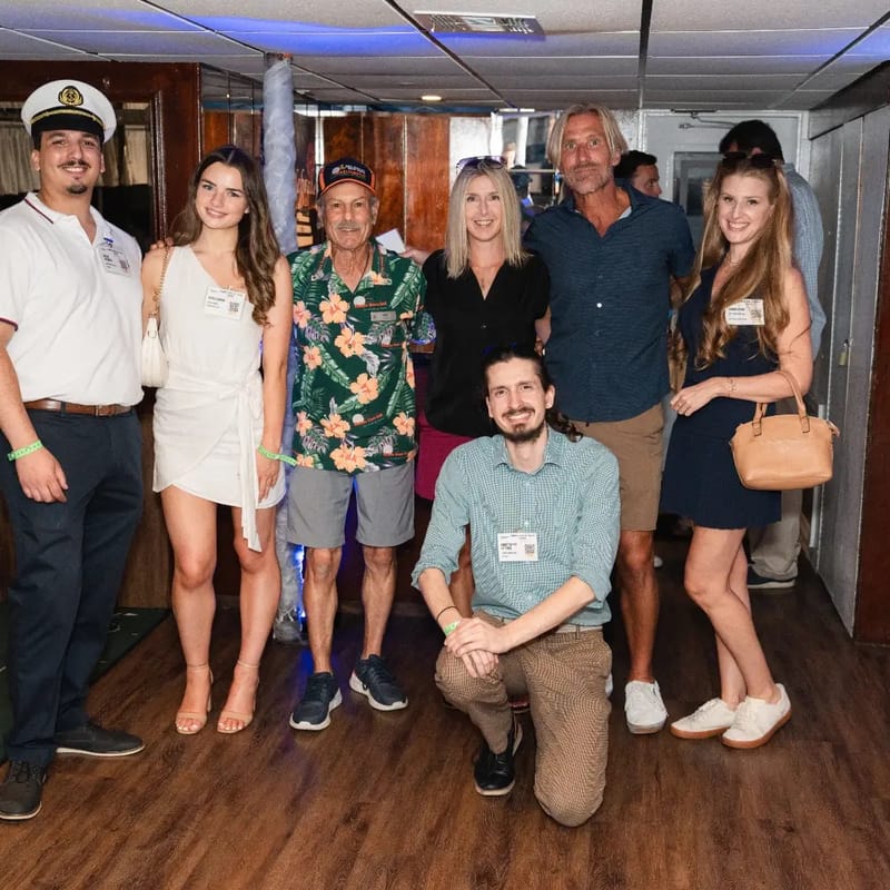 Chris Gittings kneeling in front of a group of seven guests inside the yacht